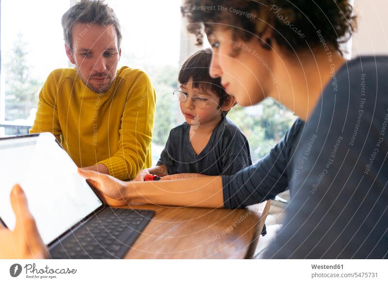 Family sitting at table, using digital tablet together father pa fathers daddy dads papa mother mommy mothers ma mummy mama son sons manchild manchildren