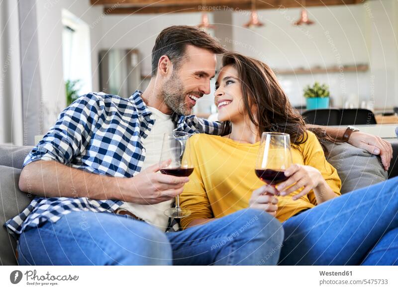 Happy couple sitting in living room, drinking red wine couch settee sofa sofas couches settees Seated living rooms livingroom twosomes partnership couples
