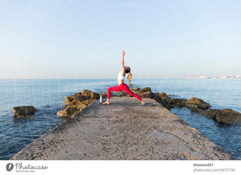 Young woman practicing yoga on the beach, doing warrior pose exercise exercising practice practise practising in the morning flexible Force Power Strengthy