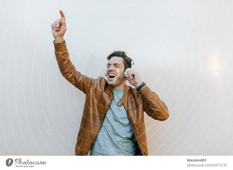 Carefree man listening to music with headphones in front of a wall headset relax relaxing hear Ardor Ardour enthusiasm enthusiastic excited delight enjoyment