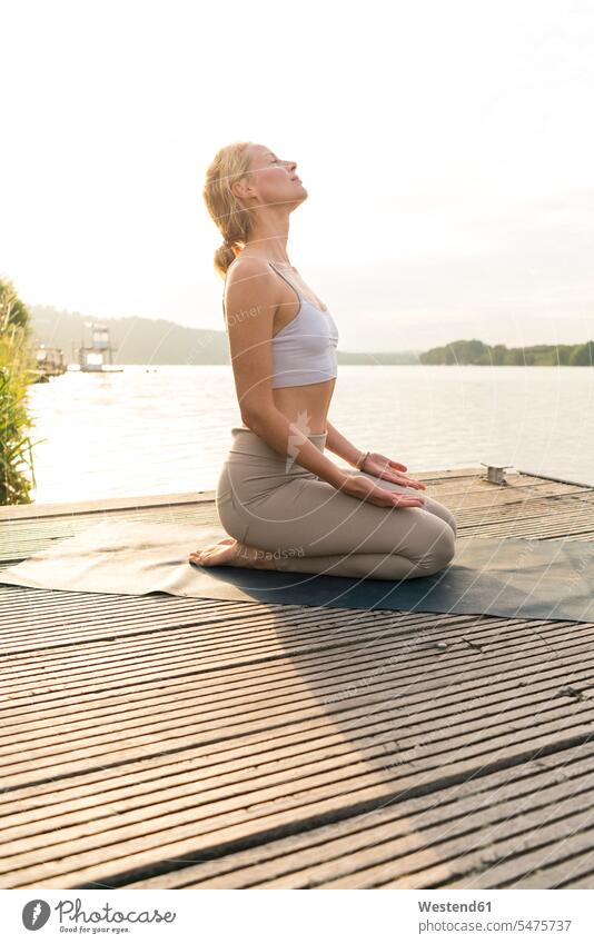 Young woman practicing yoga on a jetty at a lake towels relax relaxing exercise exercising practice practise practising in the morning summer time summertime