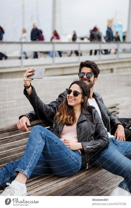Spain, Barcelona, happy young couple resting on a bench taking a selfie benches Selfie Selfies happiness twosomes partnership couples people persons human being