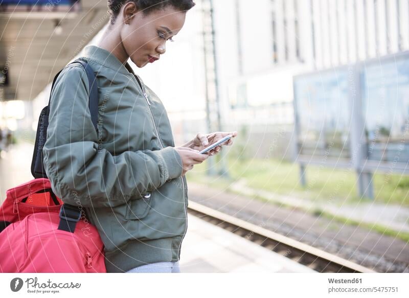 Young woman standing on platform looking at cell phone eyeing Smartphone iPhone Smartphones females women Railroad Platform view seeing viewing mobile phone