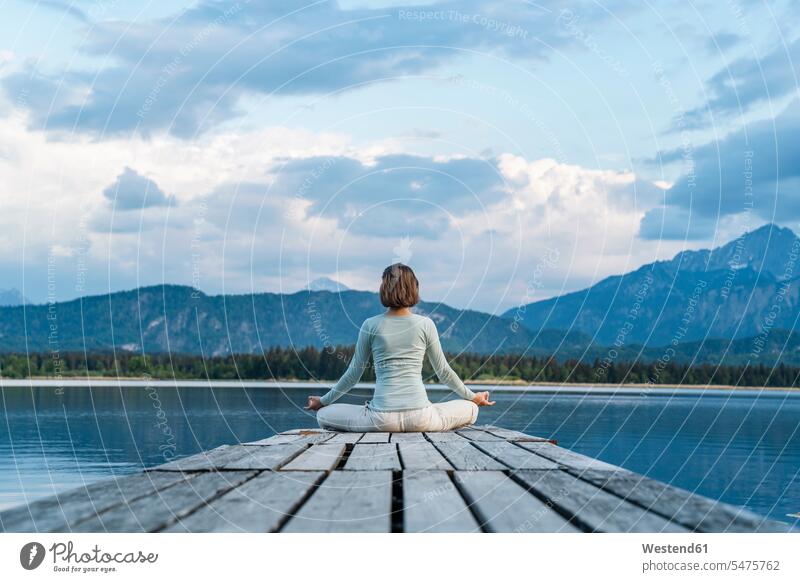 Mid adult woman meditating while sitting on jetty over lake against cloudy sky color image colour image Germany leisure activity leisure activities free time