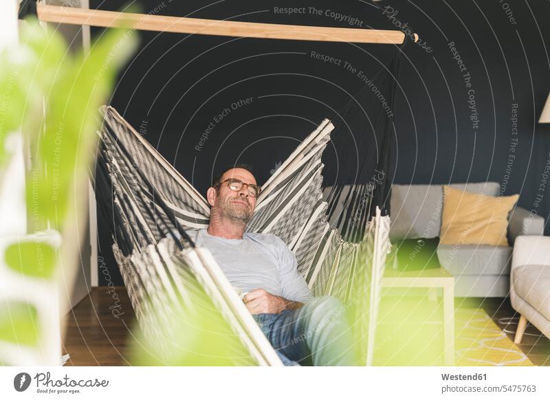 Mature man sleeping on hammock in living room at home color image colour image Germany leisure activity leisure activities free time leisure time