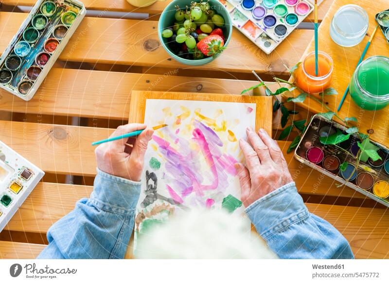 Senior man painting on paper at wooden table color image colour image indoors indoor shot indoor shots interior interior view Interiors day daylight shot