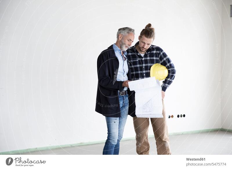 Architect and construction worker discussing blueprint while standing in empty house color image colour image Germany Architecture construction site