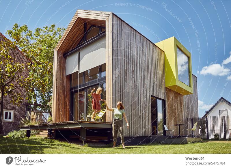 Mother assisting daughter in jumping outside tiny house at yard color image colour image Germany leisure activity leisure activities free time leisure time