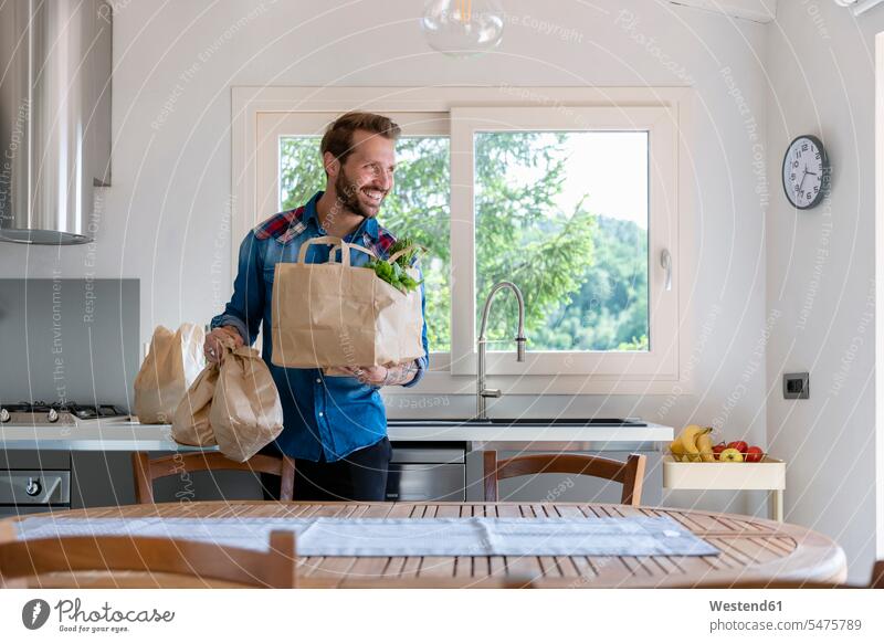 Smiling handsome man holding groceries bag while looking away in kitchen at home color image colour image indoors indoor shot indoor shots interior