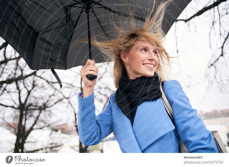 Smiling blond woman holding umbrella in storm scarfs scarves Brolly umbrellas smile delight enjoyment Pleasant pleasure Cheerfulness exhilaration gaiety gay