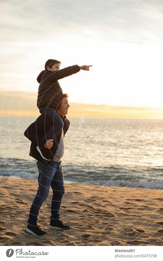 Father carrying son piggyback on the beach at sunset pointing finger sunsets sundown point at pointing at piggy-back pickaback Piggybacking Piggy Back father pa