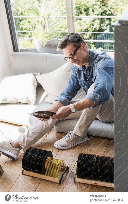 Mature man sitting at home, looking at vintage sigle recors windows couches settee settees sofa sofas Eye Glasses Eyeglasses specs spectacles records