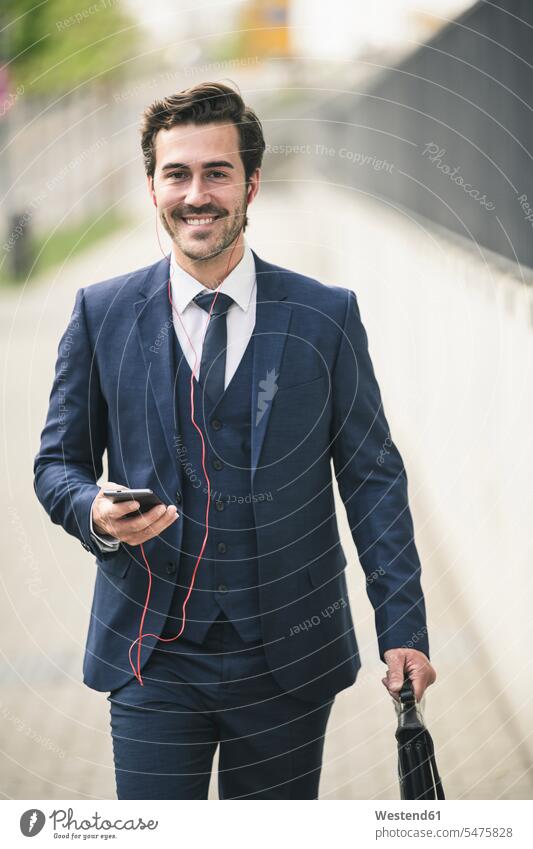 Businessman walking in the city with cell phone and earphones freelancer freelancing business business world business life urban urbanity independence