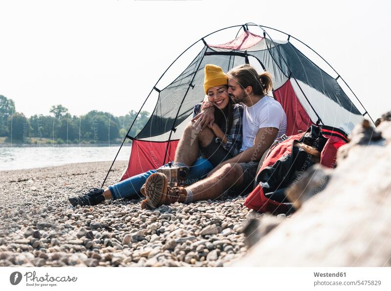 Happy young couple sitting at a tent at the riverside twosomes partnership couples tents riverbank happiness happy Seated smiling smile people persons