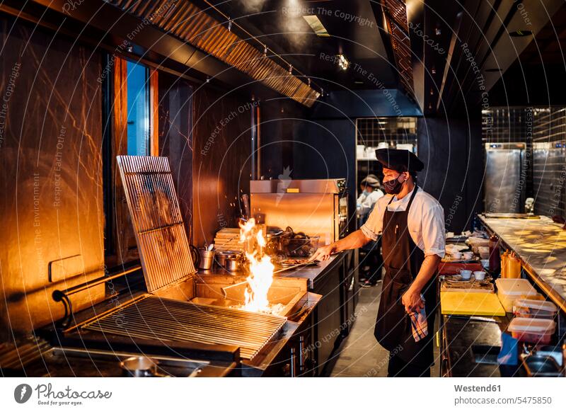 Chef wearing protective face mask preparing grill in restaurant kitchen human human being human beings humans person persons 1 one person only only one person