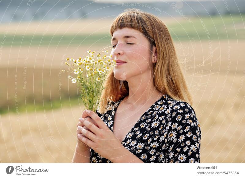 Smiling young woman with eyes closed smelling bunch of chamomile flower in nature human human being human beings humans person persons adult grown-up grown-ups