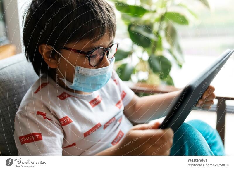 Boy with surgical mask sitting on armchair using digital tablet human human being human beings humans person persons caucasian appearance caucasian ethnicity