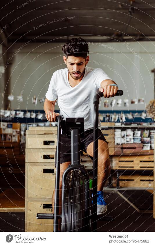 Young sportsman exercising on airbike at gym color image colour image indoors indoor shot indoor shots interior interior view Interiors day daylight shot