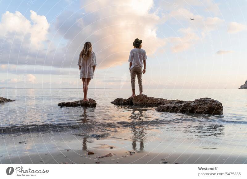 Back view of young couple standing on rocks in front of the sea watching airplane, Ibiza, Balearic Islands, Spain Air Vehicle Air Vehicles aircrafts aeroplane