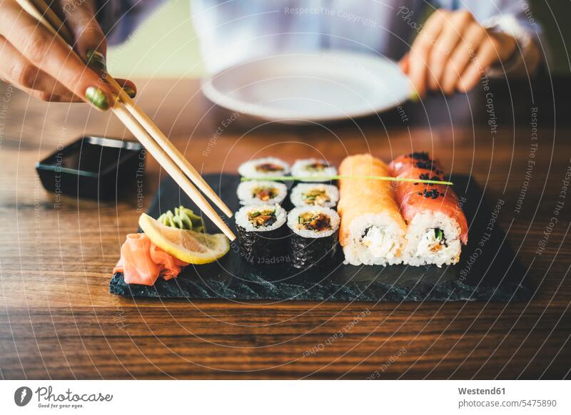 Close-up of a woman eating sushi in a restaurant dish dishes Plates Tables wood wood table hold Seated sit free time leisure time cafes cafeteria cafeterias