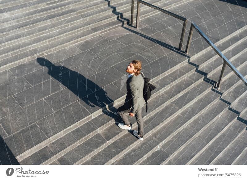 Male entrepreneur with bag moving up on staircase while looking away in downtown during sunny day color image colour image outdoors location shots outdoor shot