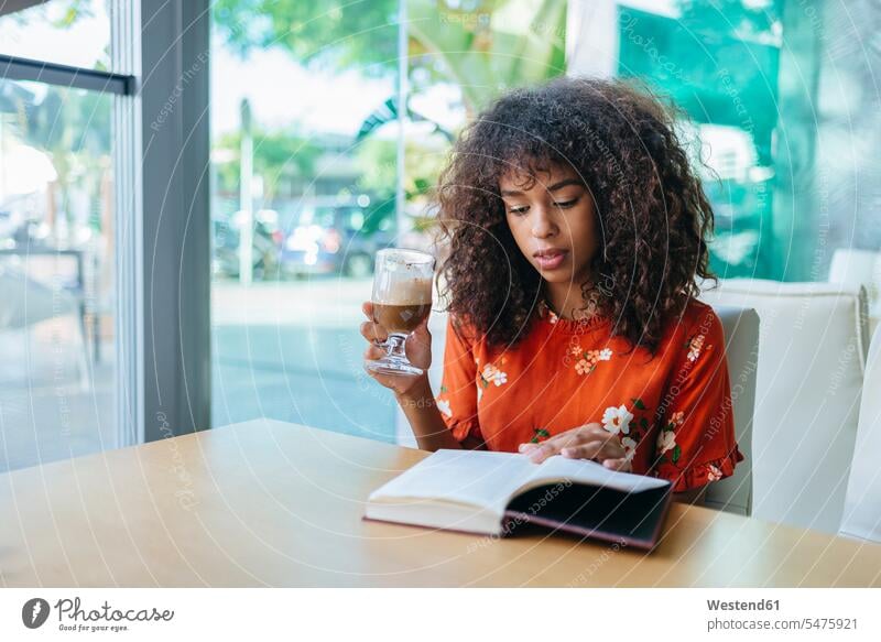 Portrait of young woman drinking coffee in a cafe while reading a book books Coffee portrait portraits females women Drink beverages Drinks Beverage
