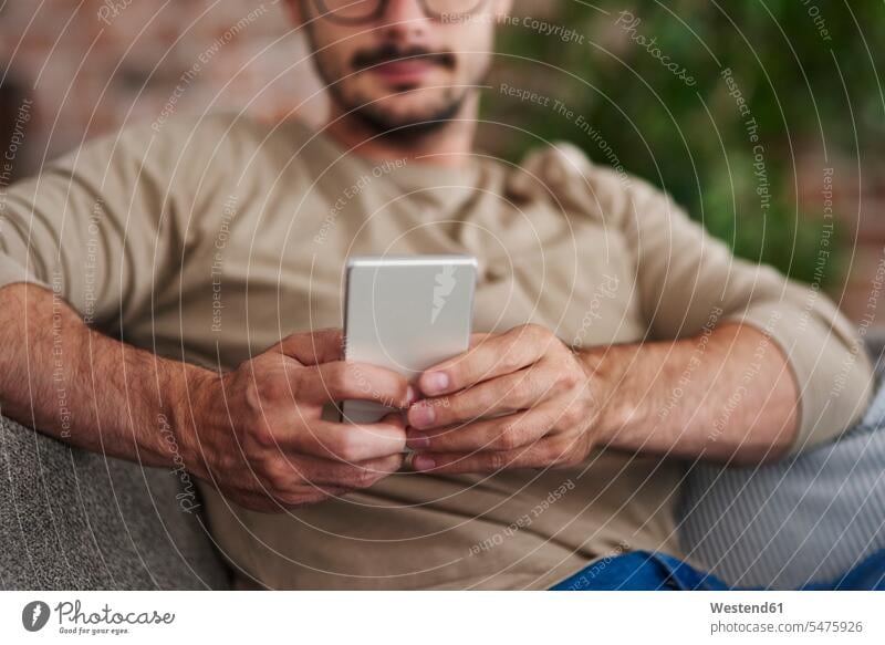 Man sitting on couch text messaging, partial view man men males home at home SMS Text Message Seated settee sofa sofas couches settees Adults grown-ups grownups