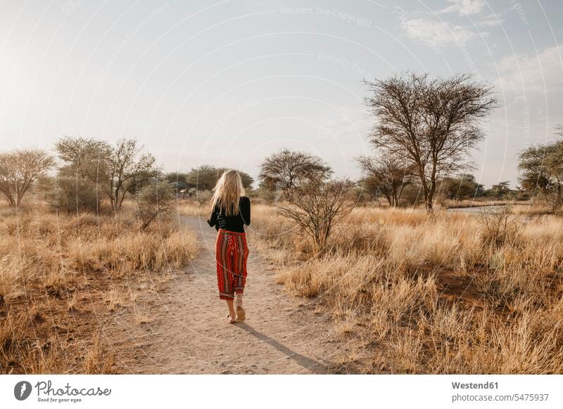 Africa, Namibia, blonde woman walking on way in grassland going females women rear view back view view from the back Traveller Travellers Travelers leaving