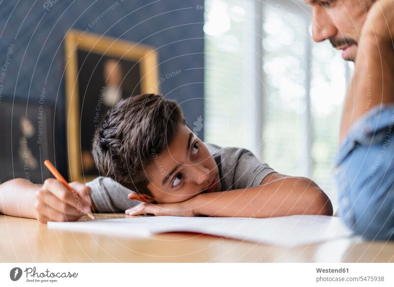 Father helping son doing homework pupils schoolchild schoolchildren Tables pencil pencils pens learn write Seated sit at home controlling Lifestyle supporting