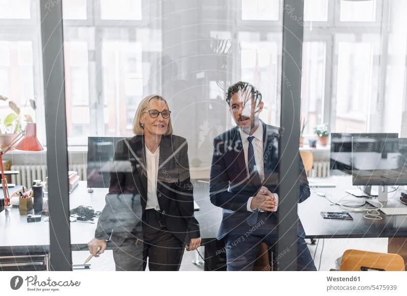 Businessman and businesswoman looking at drawing on glass pane in office human human being human beings humans person persons caucasian appearance