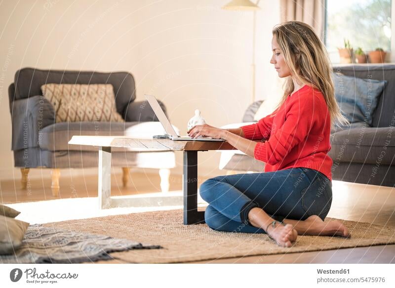 Woman using laptop on coffee table at home Coffee Table Coffee Tables Laptop Computers laptops notebook floor floors woman females women computer computers