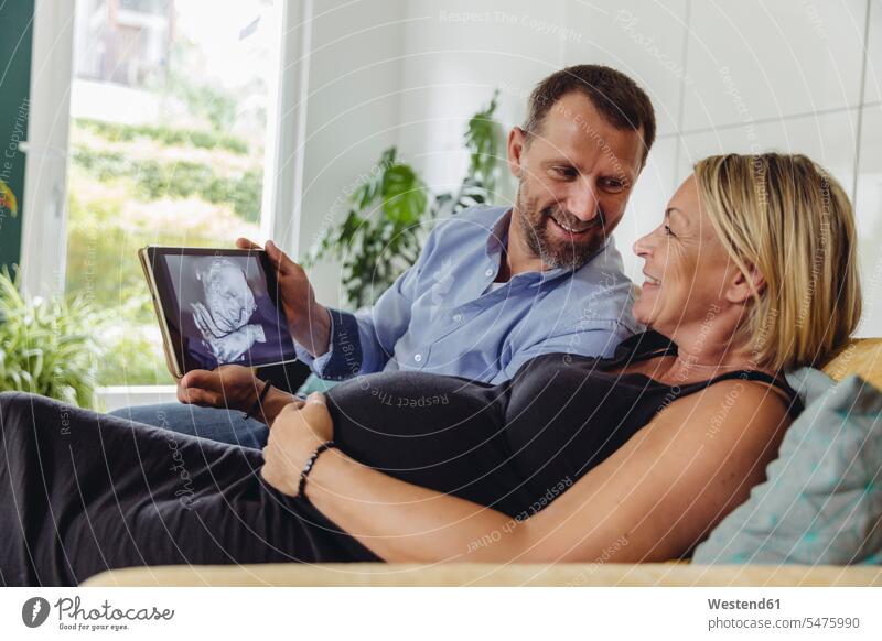 Mature pregnant couple watching a 3D image of their unborn child on tablet computer Pregnant Woman looking eyeing images picture pictures view seeing viewing