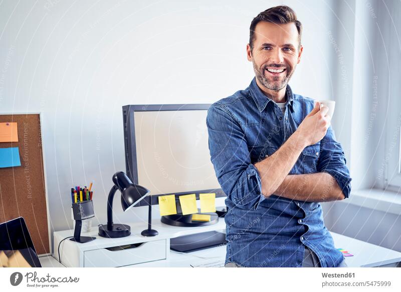 Portrait of smiling man with cup of coffee at desk in office portrait portraits men males Coffee desks offices office room office rooms smile Adults grown-ups