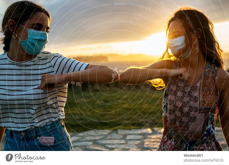 Young women in protective face masks elbow bumping against sky during COVID-19 color image colour image outdoors location shots outdoor shot outdoor shots Spain