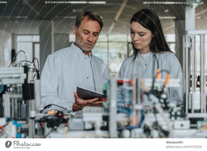 Colleagues discussing over digital tablet while standing by machinery in laboratory color image colour image indoors indoor shot indoor shots interior