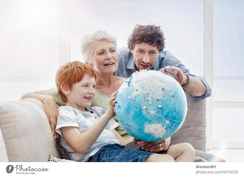 Grandmother, father and grandson sitting on couch in a villa looking at globe generation windows globes couches settee settees sofa sofas smile Seated delight