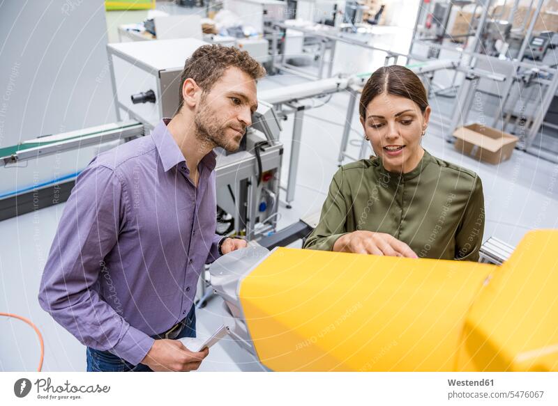 Businessman and woman having a meeting in front of industrial robots in a high tech company team checking Test testing Check explaining high-tech maintenance