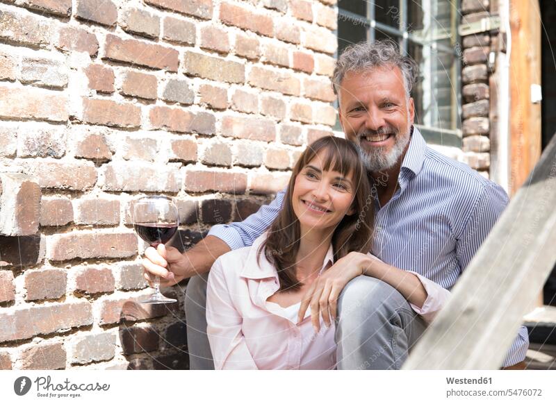 Mature couple sitting on stairs, drinking wine brick wall stairway Seated twosomes partnership couples laughing Laughter happiness happy brick walls people