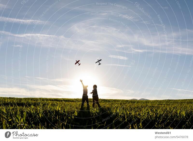 Playful brothers flying airplane toy while standing on grass in meadow color image colour image outdoors location shots outdoor shot outdoor shots day