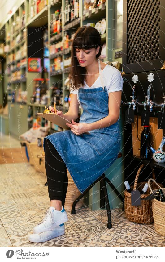 Woman sittting on stool in a store taking notes sitting Seated shop woman females women stools making a note note taking retail trade trading Adults grown-ups