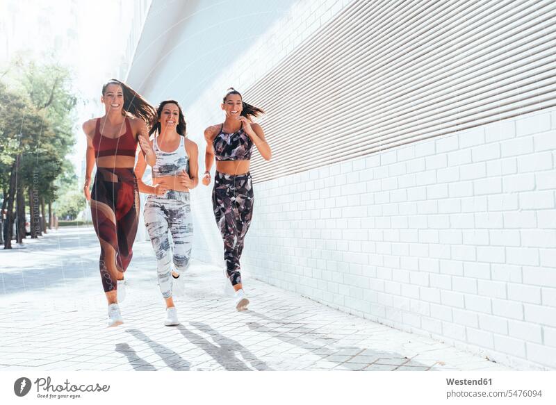 Rear view of three sporty young women running in the city friends mate female friend exercise practising train training smile summer time summertime summery