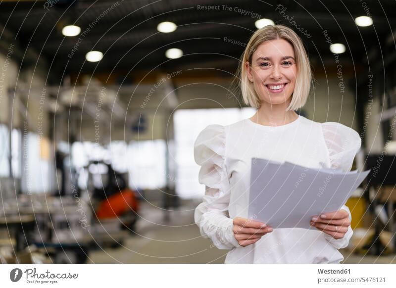 Portrait of a smiling young woman holding papers in a factory human human being human beings humans person persons caucasian appearance caucasian ethnicity