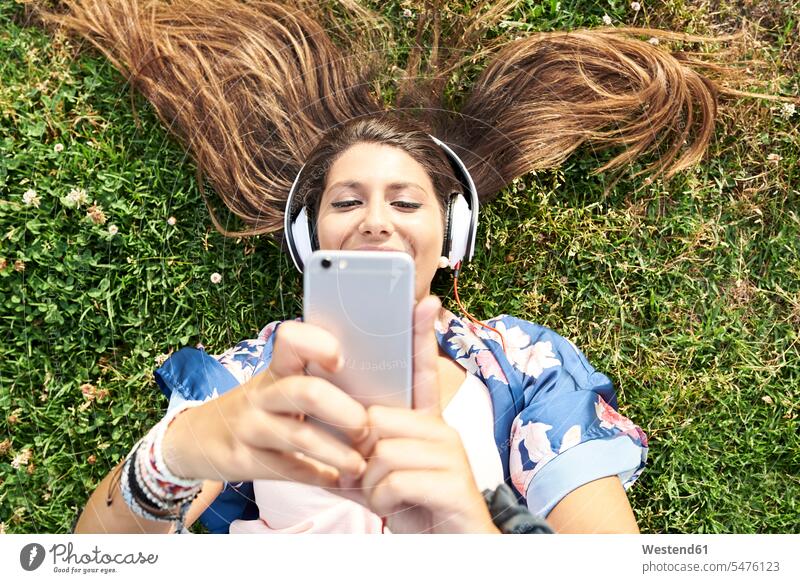 Portrait of smiling woman lying on a meadow listening music with headphones and smartphone females women portrait portraits laying down lie lying down meadows