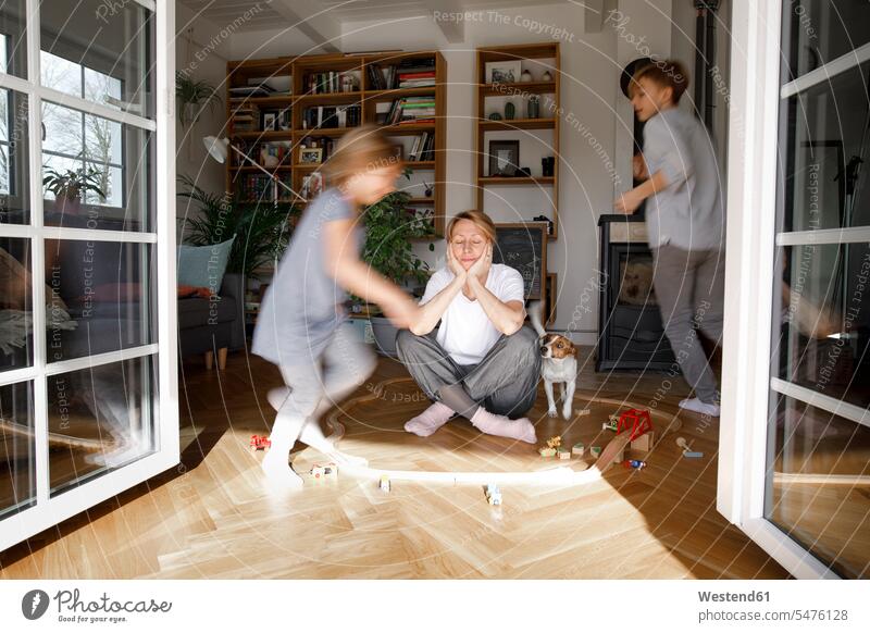 Stressed out mother sitting in the middle of toys, while children are running around her Seated play circles circular at home opened Tempo stressed stressed out