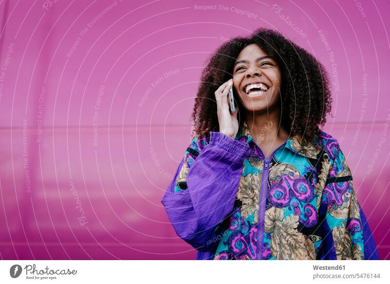 Smiling woman talking on the phone, pink wall in the background coat coats jackets telecommunication phones telephone telephones cell phone cell phones