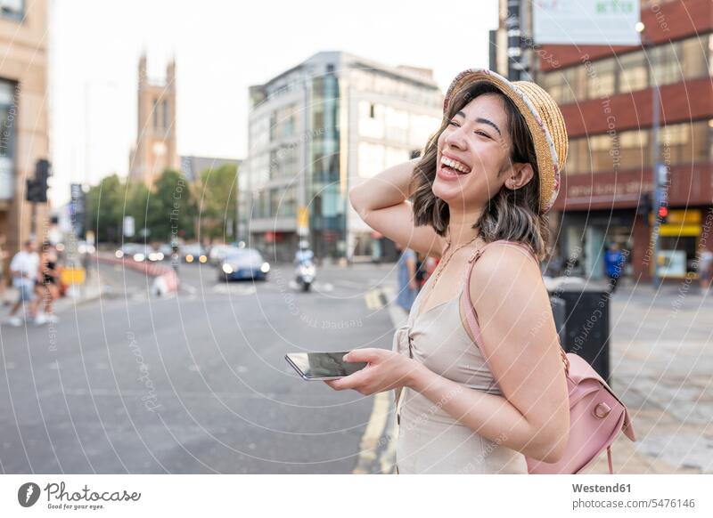 Woman laughing while using smart phone standing on street in city color image colour image outdoors location shots outdoor shot outdoor shots day daylight shot
