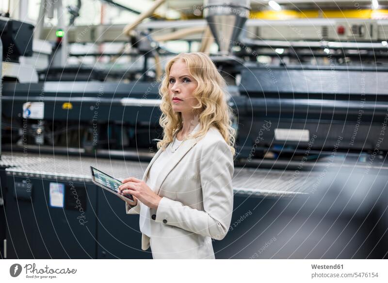 Woman with tablet at machine in factory shop floor looking around industrial hall factory hall industrial buildings woman females women factories looking round