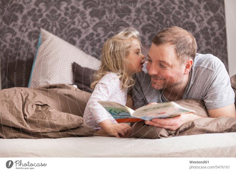 Father and daughter reading a book in bed, whispering in ear books Bed - Furniture beds hear smile speak speaking talk happy Contented Emotion pleased