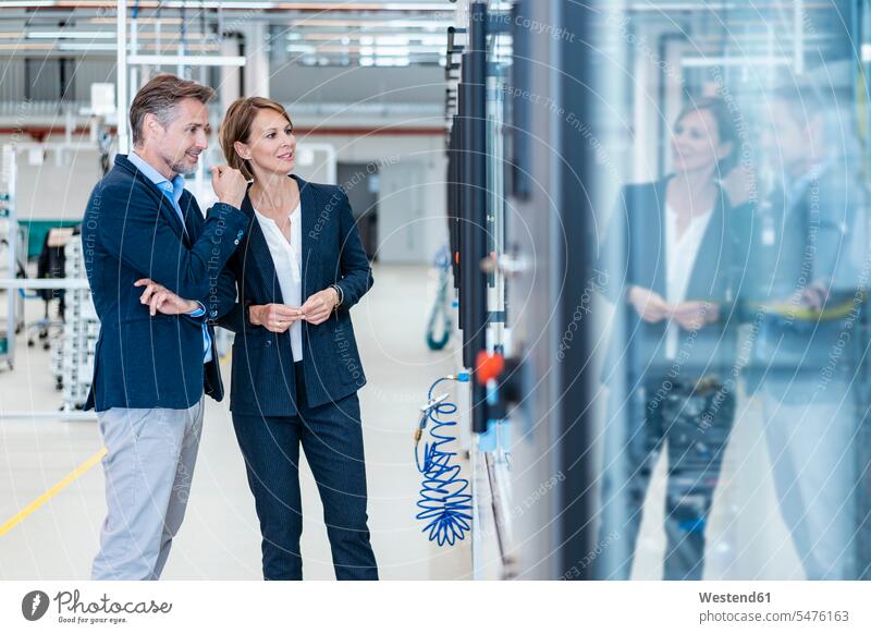 Businessman and businesswoman looking at a machine in a modern factory hall business life business world business person businesspeople associate associates
