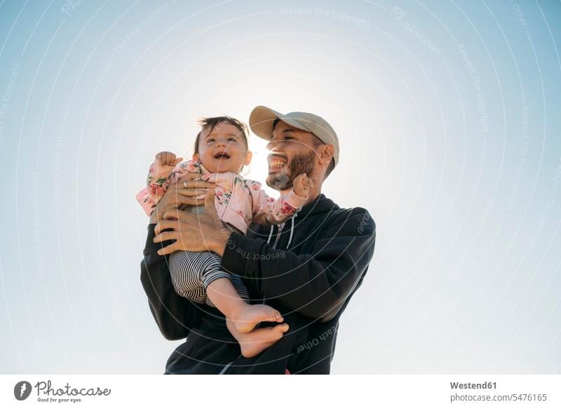 Laughing father holding baby girl at backlight baby girls female pa fathers daddy dads papa laughing Laughter infants nurselings babies people persons